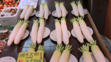 Düzgün düzenlenmiş daikon turpları bir market tezgahında sergileniyor. Fiyat tabelaları, taze sebzeler geleneksel üretim pazarında satışa sunuluyor.
