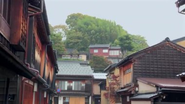 Kanazawa, JAPONYA, 17 Kasım 2010 - Tarihi bölgede kiremitli çatıları olan geleneksel ahşap binalar, yemyeşil ağaçlarla çevrili yamaçlardaki evler ve arka planda sonbahar yaprakları