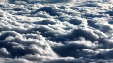 Uçaktan bulutların havadan görünüşü, gökyüzüne yayılan yumuşak bulutlar, güneş ışığı bulutların üzerine nazikçe parıldıyor.