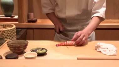 Suşi şefi karidesi bıçakla dilimliyor, ahşap tezgahta kusursuz ve yetenekli hareketler, geleneksel Japon aşçılık pratiği, otantik hazırlık