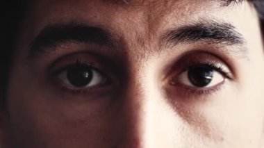 Bir adamın gözlerine yakın çekim, tarafsız ve sakin bir yüz ifadesi sergiliyor. Bakışları sabit, çevresindekileri yansıtırken sessiz bir gözlem ve farkındalık hissi veriyor.