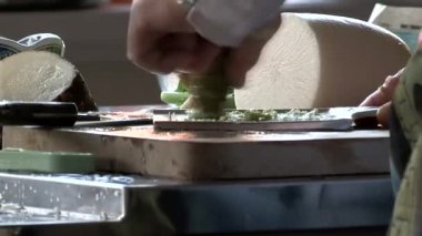 Geleneksel seramik rende taze wasabi kökü rendelemek, mutfakta keskin yeşil macun hazırlamak, Japon yemekleri, ahşap tahta üzerinde çalışan eller, yemek hazırlığı.
