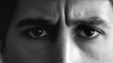 Kaşları çatık, siyah ve beyaz bir adamın gözleri yoğun ve ciddi bir ifade sergiliyor. Bakışlarına odaklanmak derin düşüncelere, konsantrasyona, güçlü duygulara işaret eder.