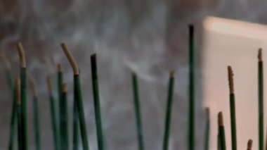 Tütsü çubuklarının yakın çekimi, dumanın havada dolaşması, huzurlu ve meditasyon yapan bir ortam, dinginlik ve yavaş yanan tütsü çubukları üzerine odaklanmak.