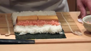 Şef bambu hasırında suşi rulosu hazırlıyor, eller nori ve pilavın malzemelerini birleştiriyor, geleneksel Japon mutfağı, hassas mutfak tekniği, taze yemek.