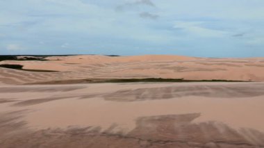 Geniş kum tepecikleri, ince desenli, bulutlu bir gökyüzünün arka planına kurulmuş, sürekli değişen çöl manzarasını gözler önüne seriyor.