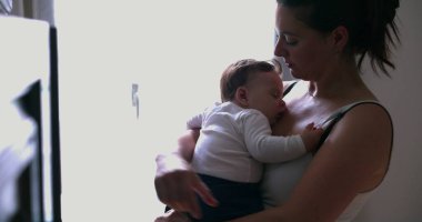 Bir annenin, uyuyan bebeğini kucakladığı, sessiz bir evde sevgi ve güvenlik sağladığı, pencerenin ışıklarıyla hafifçe aydınlattığı o hassas an.