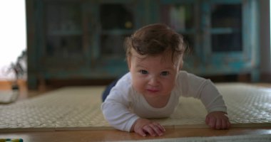 Bebek karnının üstünde, yerden yukarı bakıyor, merakını ve hayal kırıklığını ifade ediyor, rahat bir ev ortamında emekleme ve keşiflerin ilk aşamalarında yer alıyor.