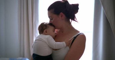 Anne bebeğini kucağında tutuyor, bebeği huzurlu bir ortamda nazikçe kucaklıyor ve rahatlatıyor, sıcaklığı ve bağlantıyı vurguluyor.