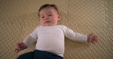 Bebek yumuşak bir paspasın üzerinde sırt üstü uzanıyor, ev ortamında sakin ve rahat görünüyor, evde dinlenirken gelişimin ilk aşamalarını ve memnuniyetini gösteriyor.