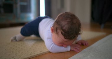 Bebek yüzüstü yerde yatıyor, üzgün ve ağlıyor, evde yumuşak bir paspasın üzerinde hayal kırıklığını ve rahatsızlığı ifade ediyor, duygusal gelişimin ilk aşamalarını vurguluyor.