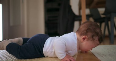 Bebek yüzüstü yatar, kafası hayal kırıklığına uğrar, huzurlu bir ev ortamında yumuşak bir paspas üzerinde emekleme girişiminde bulunurken duygularını ifade eder.