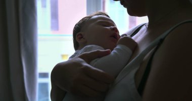 Bebeğin kollarında huzurlu bir şekilde uyuması için bebeğini kucağına alıp sıcak ve güvenli bir yere götüren bir annenin yakın çekimi.