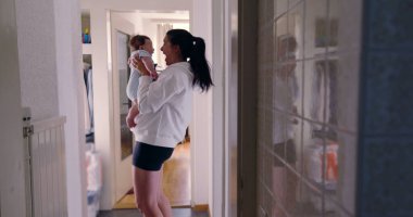 Anne koridorda karoları yansıtarak bebeği tutuyor, samimi otantik yaşam tarzı sahnesi, samimi aile anı, beslenme ve bağ kurma, sıcak ve doğal ışık