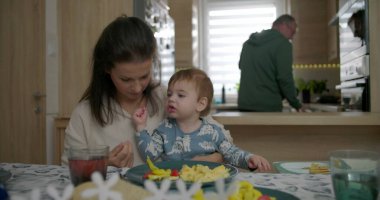 Anne kahvaltı masasında bebeği besliyor, bebekle kaynaşıyor çırpılmış yumurta ve sebzeleri keşfediyor, sıcak mutfak ortamında aile bağlarını besliyor.