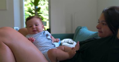 Anne bebekle kanepede uzanıyor, huzurlu bir evde dinleniyor, sıcak ve rahat bir oturma odasında sessiz bir bağ kurma zamanını paylaşıyor.