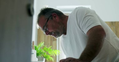 Adam lavaboda dişlerini fırçalıyor, hafifçe öne eğiliyor, temiz ve modern banyoda sabah rutininin bir parçası olarak kendine bakım ve ağız temizliğine odaklanıyor.