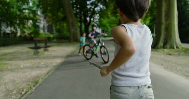 Parkta ağaçlarla kaplı bir patikada koşan çocuk, açık havada oynamanın enerjisini ve özgürlüğünü vurguluyor, büyük ağaçlar ve doğal çevreyle.