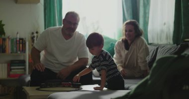 Anne ve baba kanepede oturup çocuğa gülümsüyor kahve masasında oyuncak trenle oynuyor rahat oturma odası düzeninde, neşeli aile anları, kapalı alanda kaynaşma zamanı.