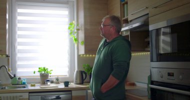 Modern mutfakta duran adam, düşünceli poz, gündelik yaşam tarzı, elleri cepte, huzurlu ev düzeni, doğal ışık ile ev rutini