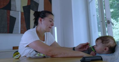 Anne bebeğini evdeki yüksek sandalyede kaşıkla besliyor, birlikte beslenme anımızı paylaşıyor.