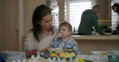 Anne kahvaltı masasında bebeği besliyor, bebekle kaynaşıyor çırpılmış yumurta ve sebzeleri keşfediyor, sıcak mutfak ortamında aile bağlarını besliyor.