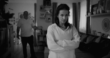 Şiddetli tartışmalar sırasında sert ifadeli bir kadının yakın çekimi, arka planda bulanık bir adam öfkeyle işaret ediyor, duygusal gerilimi yakalıyor ve çözülmemiş çatışmaları yakalıyor.