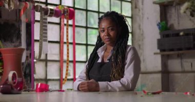 Kırsal bir çiçekçide gururla gülümseyen bayan çiçekçi, küçük işletme sahibi, iş günü zorluklarını aştıktan sonra pozitifliğini ve gururunu gösteriyor.