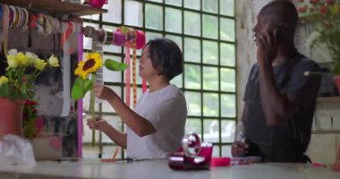 Çiçekçiler birlikte çalışarak kırsal kesimdeki çiçekçi dükkanında çiçek siparişine hazırlanırken takım çalışması ve koordinasyon düzenlerler.