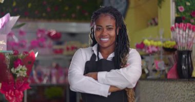 Afro-Amerikalı çiçekçi, çiçekçi dükkanında kollarını kavuşturmuş gururlu bir girişimci ya da çalışan gibi gülümsüyor.