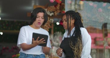 Çiçekçi dükkanının önünde fikir alışverişinde bulunurken, envanter veya tablet siparişlerini inceleyen iş arkadaşları verimli iş operasyonları üzerinde durdular.