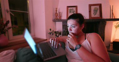 Kadın laptopuna odaklanmış, gece geç saatlere kadar çalışıyor. Yüzündeki yoğun ifade, loş bir odada ekranın parıltısıyla aydınlanan konsantrasyon ya da endişeye işaret ediyor.