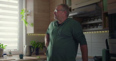 Pencerenin yanında duran adam, düşünceli poz, rahat ev hayatı, ev hayatı, modern mutfak arka planı yeşillik ve doğal ışık