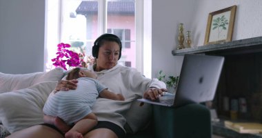 Anne dizüstü bilgisayarda çalışırken bebek göğsünde uyuyor kulaklık takıyor, rahat oturma odası, iş ve ebeveynlik dengesi, yumuşak doğal ışık.
