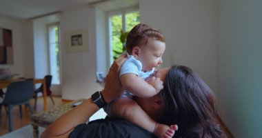 Anne ve bebek, parlak bir oturma odasında birlikte oynuyorlar. Neşeli anlar, kahkahalar ve doğal ışıklandırmayla bağ kuruyorlar.