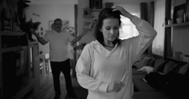 Ateşli tartışmalar sırasında kolları çapraz duran kadın kararlı ve kızgın görünürken, arka plandaki adam hayal kırıklığı içinde hareketler yapıyor, yoğun ilişki çatışmalarını yakalıyor.