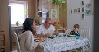 Aile yemek masasında birlikte yemek yiyor, anne babalar çocukla yemek yiyor, aile bağlarını güçlendirme anı paylaşılan yemeğe ve sohbete odaklanıyor.