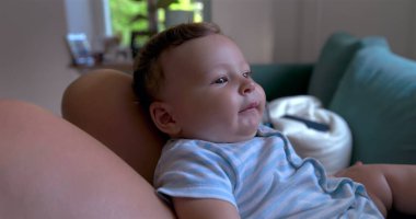 Anne oynarken bebeğini yüzüne yakın tutuyor, sıcak, aile dostu bir oturma odasında sevgi ve bağ anları, doğal ışıklandırma.