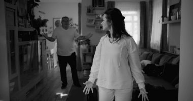 Kadın hararetli tartışmalar sırasında kafasını tutarken, arka plandaki erkek öfkeyle işaret ediyor, yoğun çatışma ve duygusal sıkıntı çekiyor..