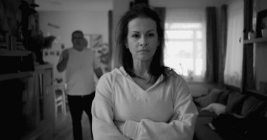 Ateşli tartışmalar sırasında kolları çapraz duran kadın kararlı ve kızgın görünürken, arka plandaki adam hayal kırıklığı içinde hareketler yapıyor, yoğun ilişki çatışmalarını yakalıyor.