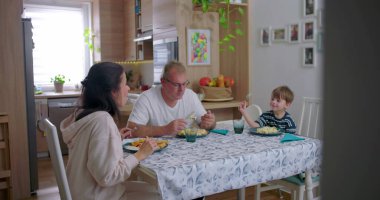 Aile yemek masasında birlikte yemek yiyor, anne babalar çocukla yemek yiyor, aile bağlarını güçlendirme anı paylaşılan yemeğe ve sohbete odaklanıyor.