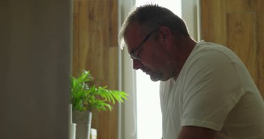 Banyo aynasının önünde düşünceli bir şekilde oturan adam, sakin bir ifadeyle yan profil görüntüsü, sessiz ve huzurlu iç mekan ortamını yansıtıyor.