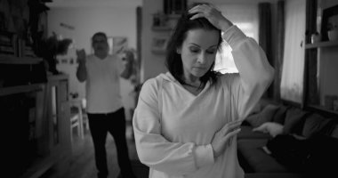 Ateşli tartışmalar sırasında kolları çapraz duran kadın kararlı ve kızgın görünürken, arka plandaki adam hayal kırıklığı içinde hareketler yapıyor, yoğun ilişki çatışmalarını yakalıyor..