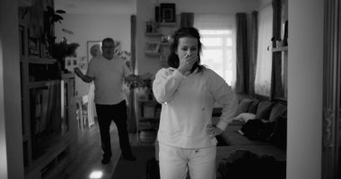 Kadın hararetli tartışmalar sırasında kafasını tutarken, arka plandaki erkek öfkeyle işaret ediyor, yoğun çatışma ve duygusal sıkıntı çekiyor..