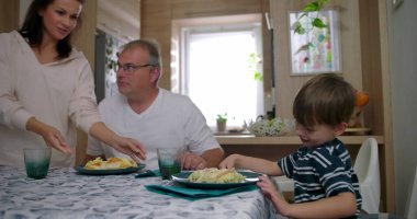 Aile masada bir yemeği paylaşır, anne bulaşıkları servis ederken baba ve oğul doğal sohbetler yapar, bağlantıyı ve sıcaklığı ön plana çıkarır.