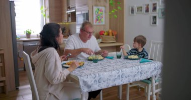Aile yemek masasında birlikte yemek yiyor, anne babalar çocukla yemek yiyor, aile bağlarını güçlendirme anı paylaşılan yemeğe ve sohbete odaklanıyor.