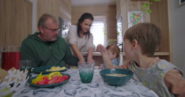 Ebeveynler aile yemeği sırasında çocuklarla etkileşim halinde, karşılama mutfağında yemek servisi ve paylaşımı, yetiştirme ve ebeveynlik bakımını vurgulayarak,