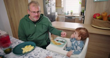 Baba, ufaklığın renkli kahvaltı tabağını meyve ve gözlemelerle keşfetmesine yardım ediyor.