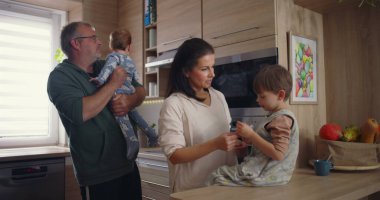 Modern mutfaktaki aile etkileşimi, baba bebeğini kucağında tutarken annesinin tezgahta oturması, sıcak aile bağlarının kurulması.