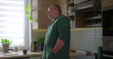 Modern mutfakta duran adam, düşünceli poz, gündelik yaşam tarzı, elleri cepte, huzurlu ev düzeni, doğal ışık ile ev rutini